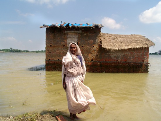 Jinsi Devi in front of her mud house that is surrounded by water with the tarpaulin on the roof which she received from CARE as part of a relief kit.